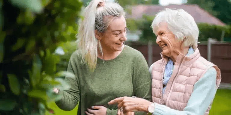 international-carer-helping-elderly-lady-around-the-garden_2x1-768x384-1.png