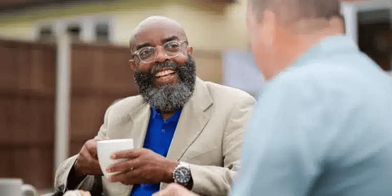 man-with-glasses-blazer-and-hot-drink-male-carer-in-foreground_2x1-768x384-1.png